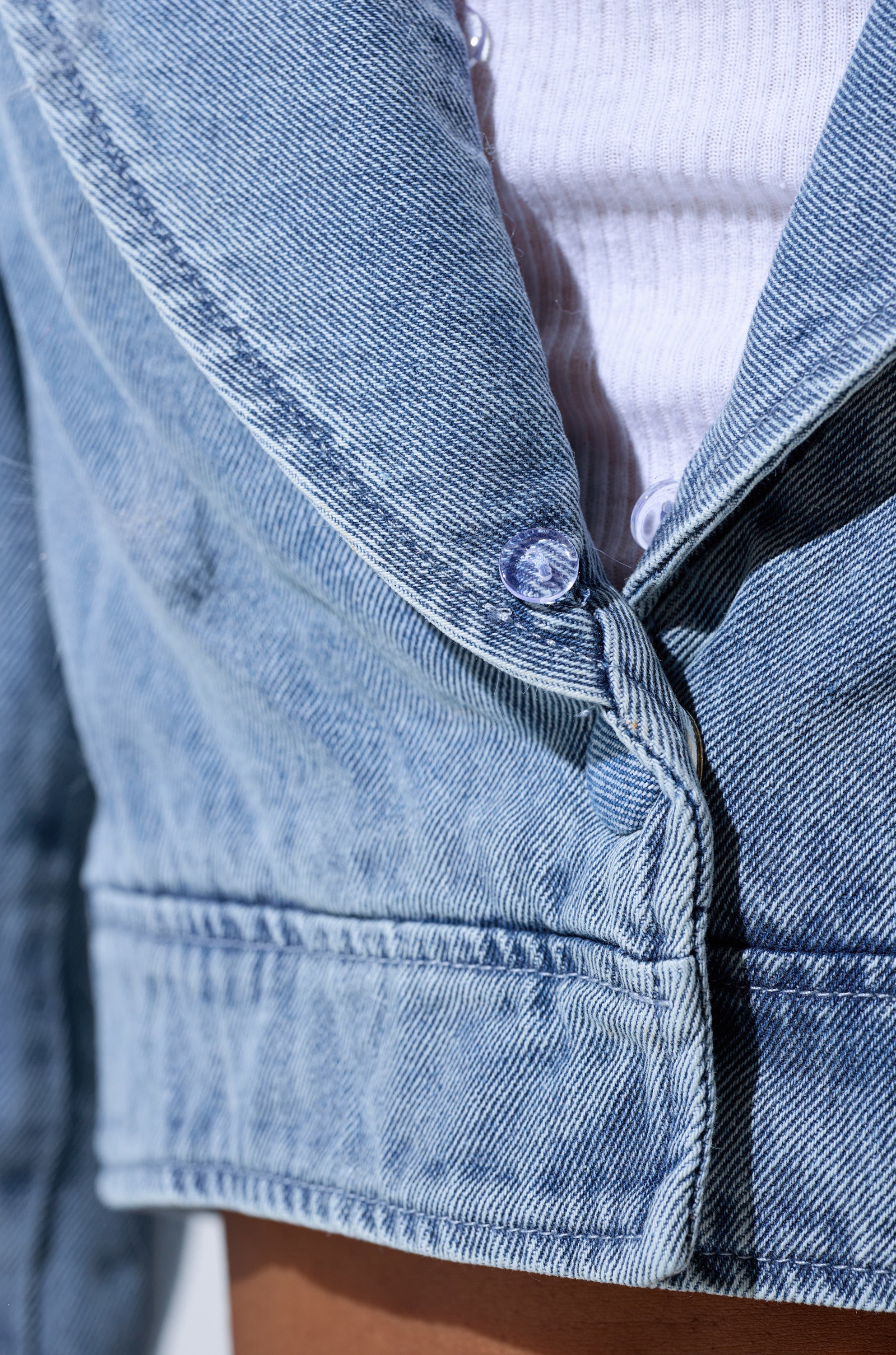 Close-up of the GISELE FUR TRIM DENIM JACKET in light blue, featuring a visible button and worn over a white ribbed shirt. The photo highlights its texture and stitching, echoing iconic Y2K and Bratz Doll-inspired style.