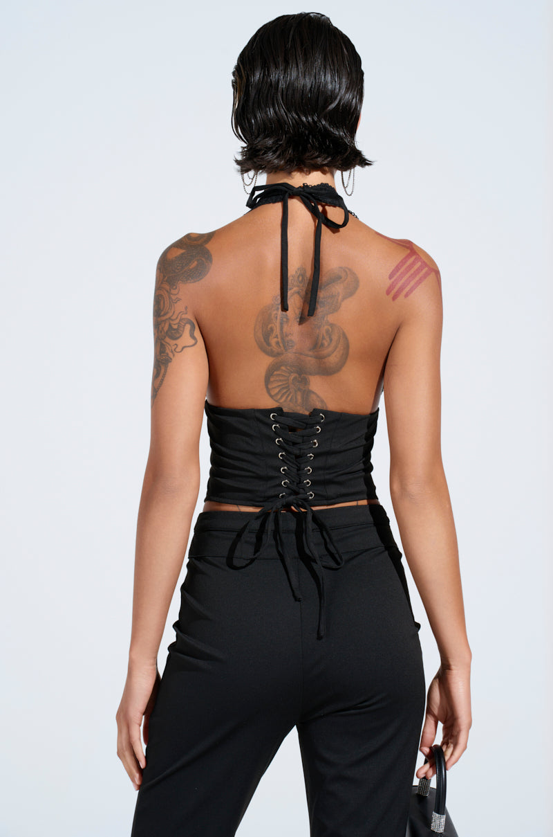 Rear view of a person with short dark hair in the FEELING EXTRA CORSET TOP, featuring a black, curve-hugging design and lace-up back. Tattoos on the left shoulder and back add an edgy vibe against a plain light background.