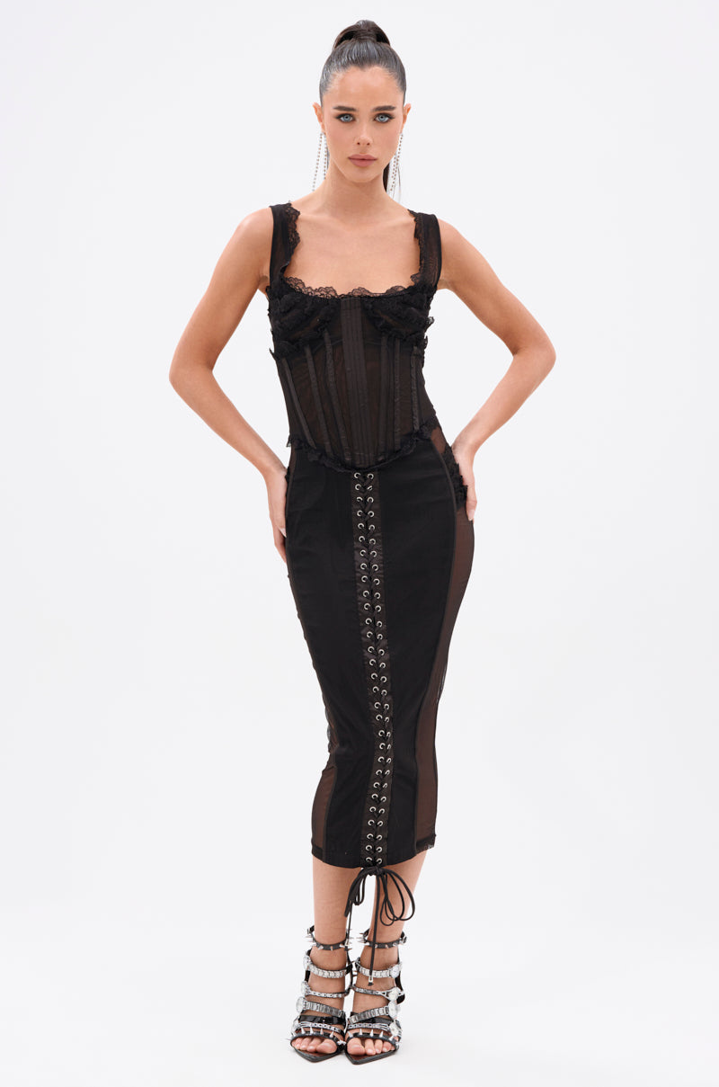 A woman with a high ponytail poses against a white background in the LET ME REMIND YOU LACE UP MESH MIDI DRESS, featuring a corset-inspired bodice and curve-hugging skirt. She completes her look with strappy high-heeled sandals.