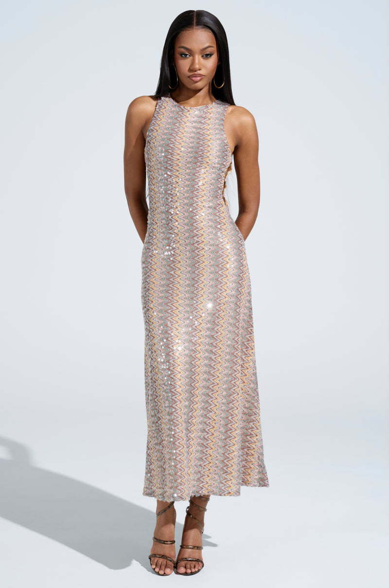 Against a light background, a person wearing the WOKE UP IN IBIZA CROCHET MIDI DRESS, shimmering with multicolors, stands elegantly. Their long hair gently cascades as strappy heels complete their confident look.