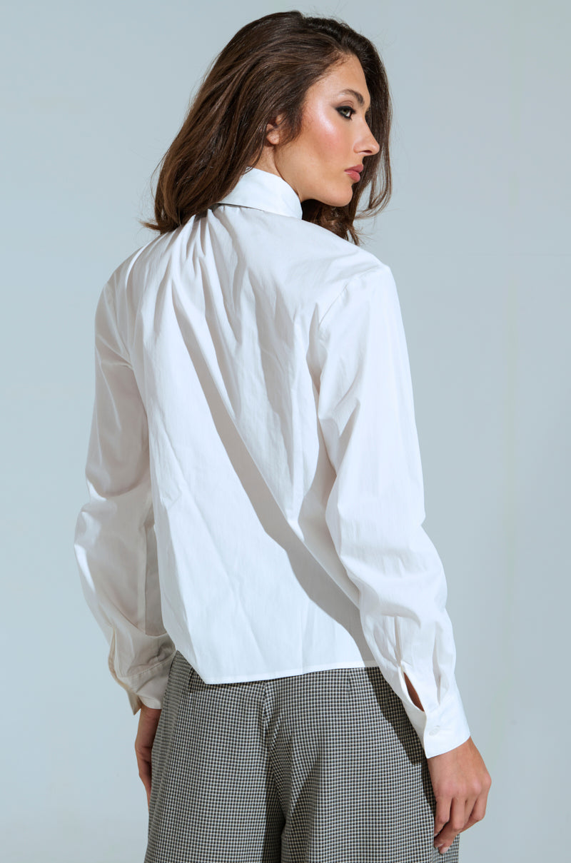 A person with long hair wears a crisp BOSS ENERGY BUTTON DOWN and checkered pants. They stand, looking to the side against a plain background, exuding confidence that mirrors the AKIRA Label's signature style.