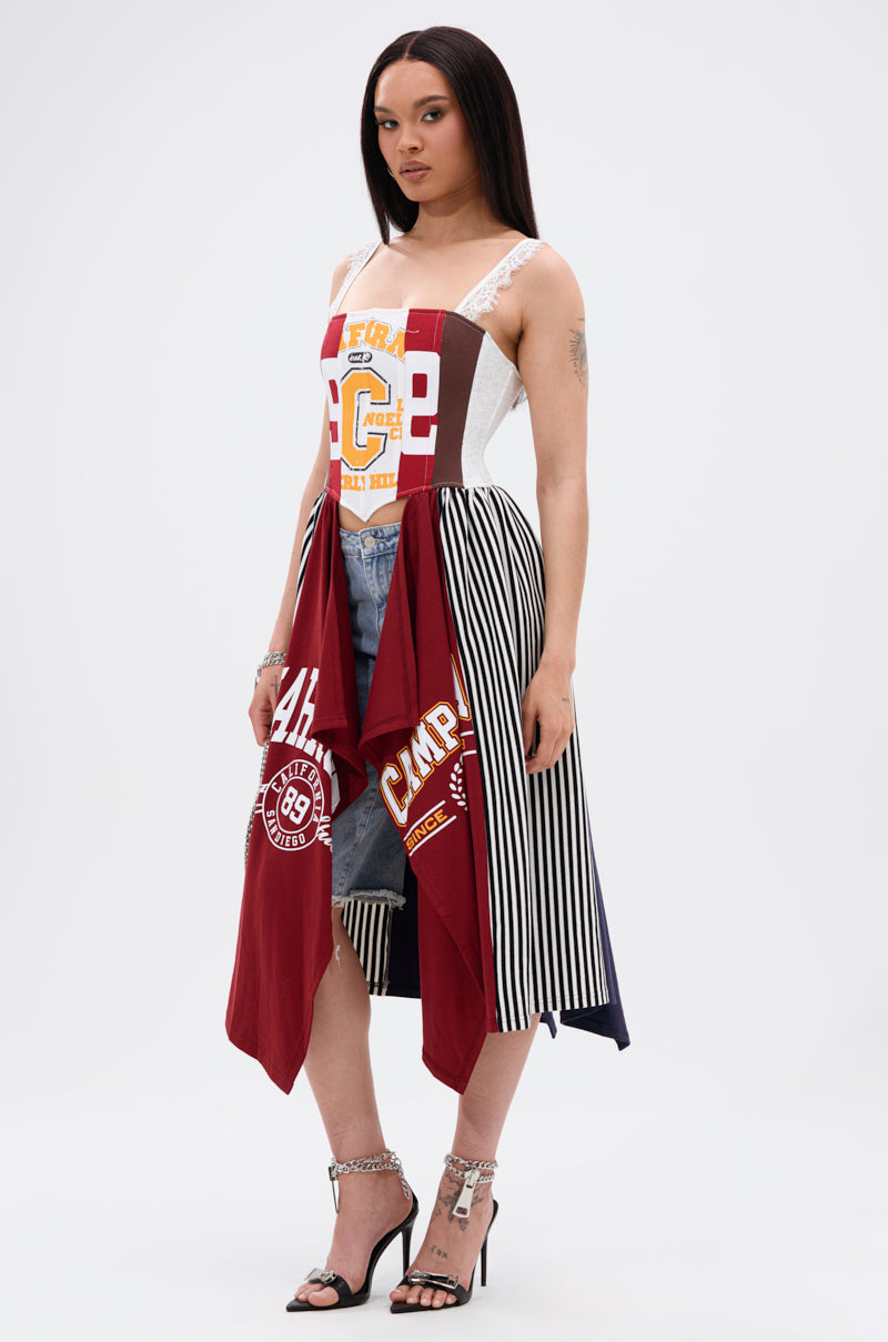 A woman wears the LIGHTS OUT PATCHED UP JERSEY CORSET—crafted from upcycled collegiate tees, with mixed fabrics, bold red graphics, black-and-white vertical stripes, lace straps—styled over denim shorts and high-heeled sandals.