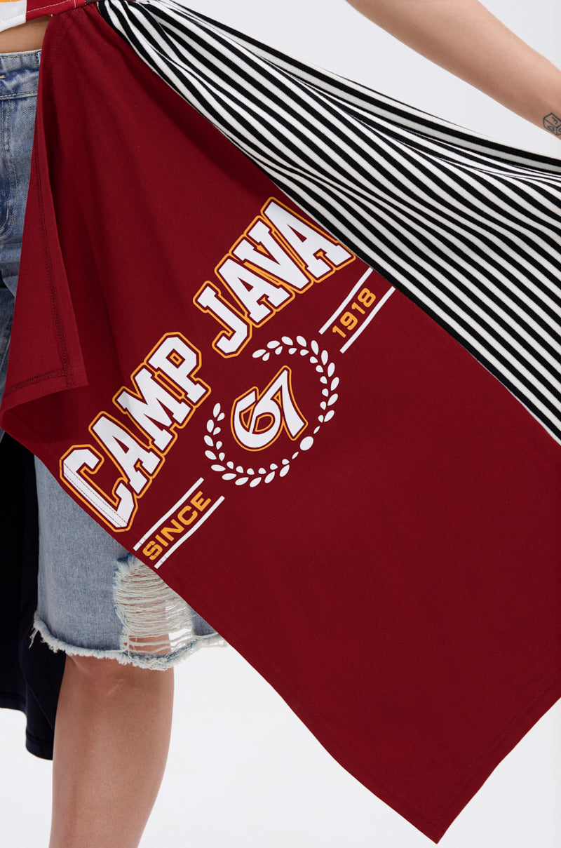 Sporting a tomboy-chic vibe, a person in frayed denim shorts holds the LIGHTS OUT PATCHED UP JERSEY CORSET—diagonally draped, made from upcycled collegiate tees with "CAMP JAVA," "SINCE 1978," "67," and black-and-white stripes.