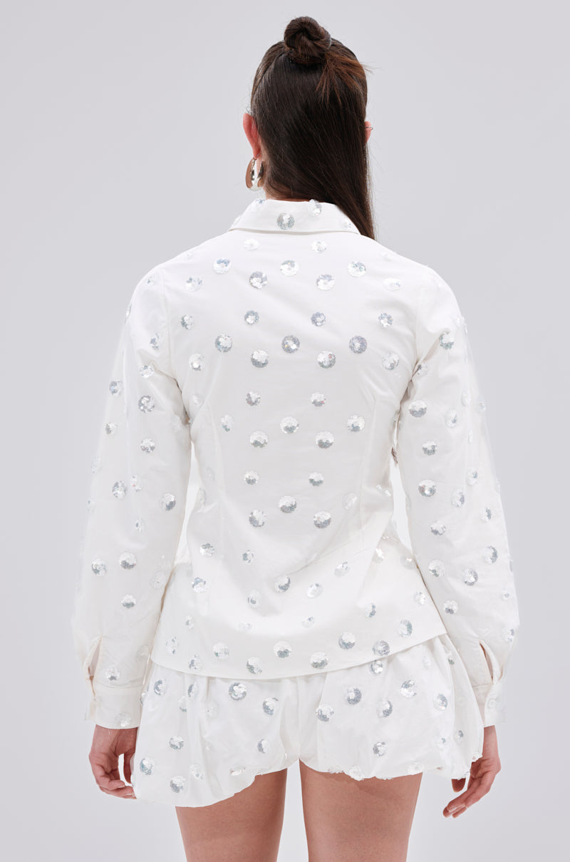 A person with long brown hair in a half-up style is seen from behind wearing the LUX FASHION BLOUSE and matching white shorts, both embellished with silver sequin dots.