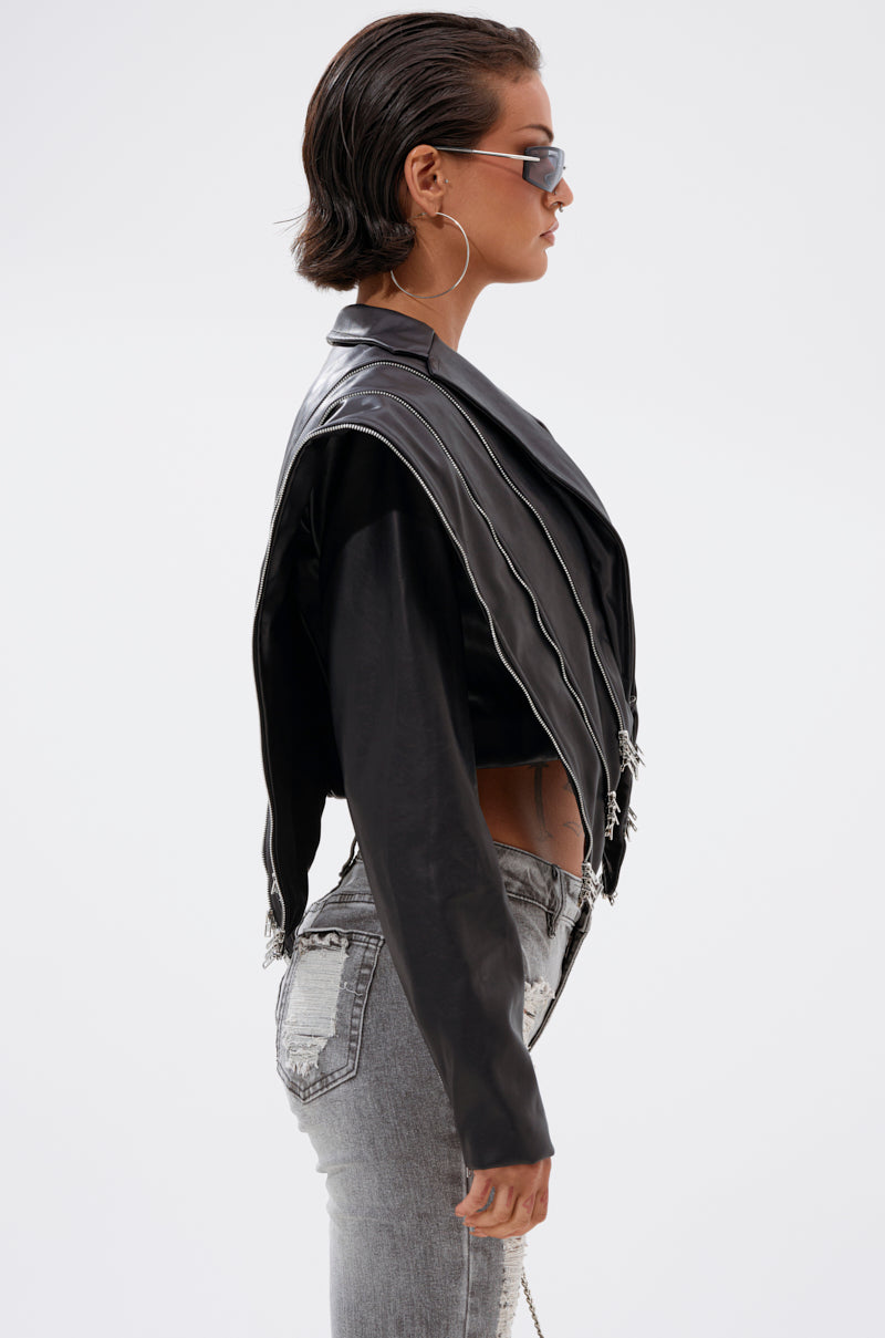 Wearing the COSMO ZIPPER MOTO—a cropped moto jacket with zipper details—this person has short, slicked-back hair, sunglasses, large hoop earrings, and light-washed jeans. They're shown in profile against a plain background.