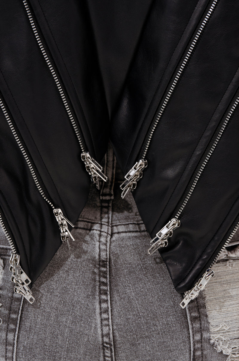 Close-up of the COSMO ZIPPER MOTO, a black faux leather jacket with multiple silver zippers in a V-shape, styled over light gray denim jeans featuring frayed edges and visible back pockets.