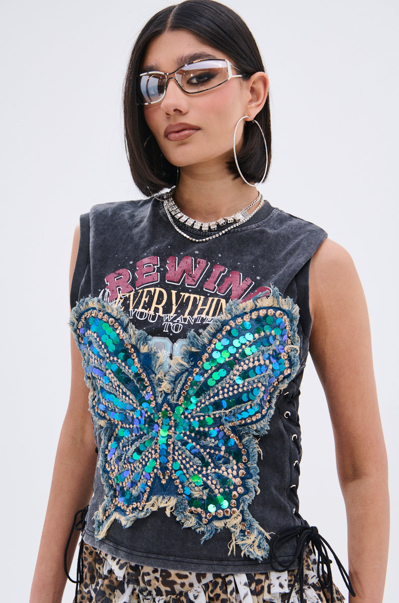 A woman wears futuristic sunglasses, hoop earrings, a REWIND EVERYTHING TEE with distressed “REWIND” text and sequined butterfly, a silver necklace, and leopard print pants.