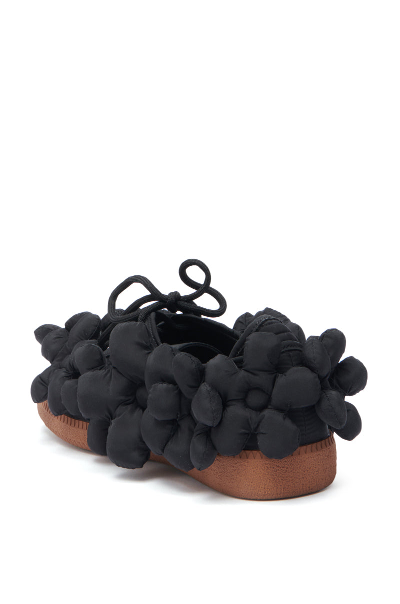 The AZALEA WANG GREYI BLACK PUFF FLORAL FLAT SNEAKER features black puffed floral fabric on the upper and a chunky textured brown sole, displayed from a rear side angle.