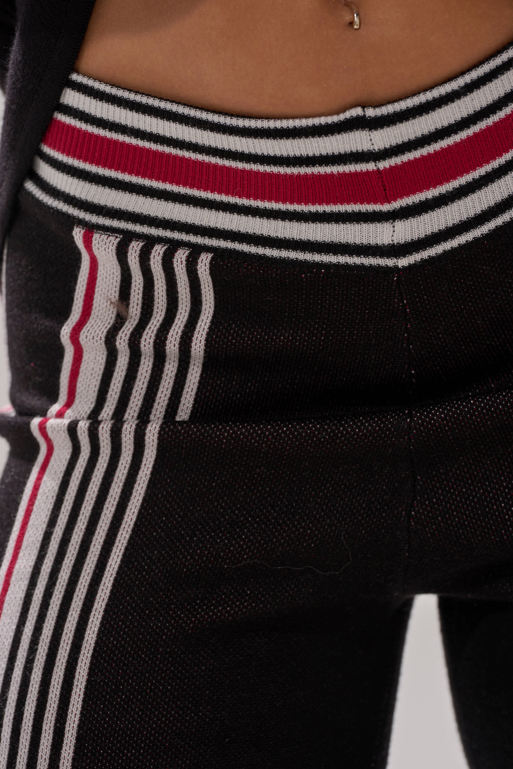 Close-up of a person wearing the KENDALL SWEATER WIDE LEG PANT, featuring high-rise, wide-leg design with vertical red and white stripes and a matching waistband; a belly button piercing is visible.