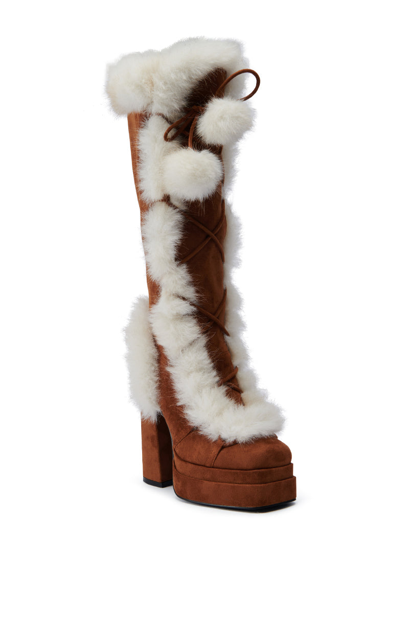 The AZALEA WANG HARIBO TAN FUR BOOT is a faux suede, brown high-heeled boot featuring white fur trim and pom-poms. Designed with laces and a chunky platform sole, this mid-calf boot boasts a tall shaft and a fashionable style that's ideal for winter wear.