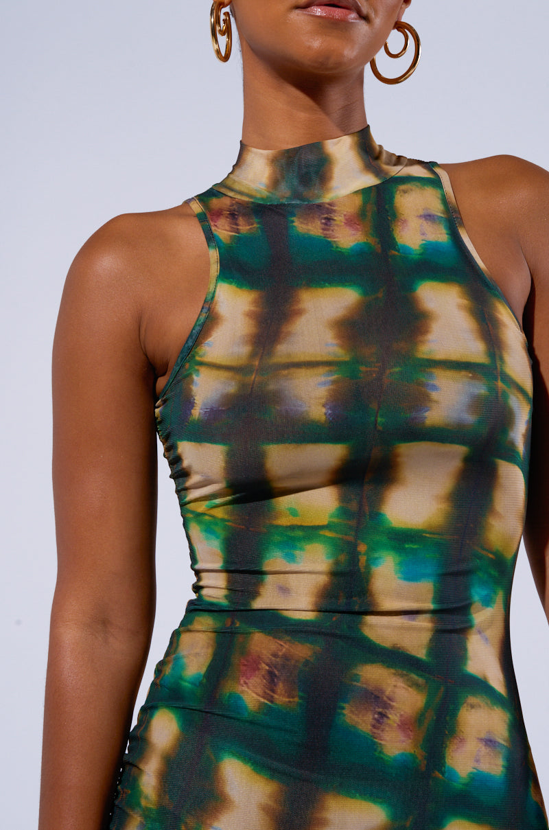 An individual is donning the COOL FOR THE SUMMER PRINTED MAXI DRESS, showcasing a sleeveless design with a high neckline and a vibrant, abstract pattern in green, yellow, and brown hues. Complemented by gold hoop earrings, they are depicted in a photograph cropped from the shoulders to the waist against a neutral backdrop.