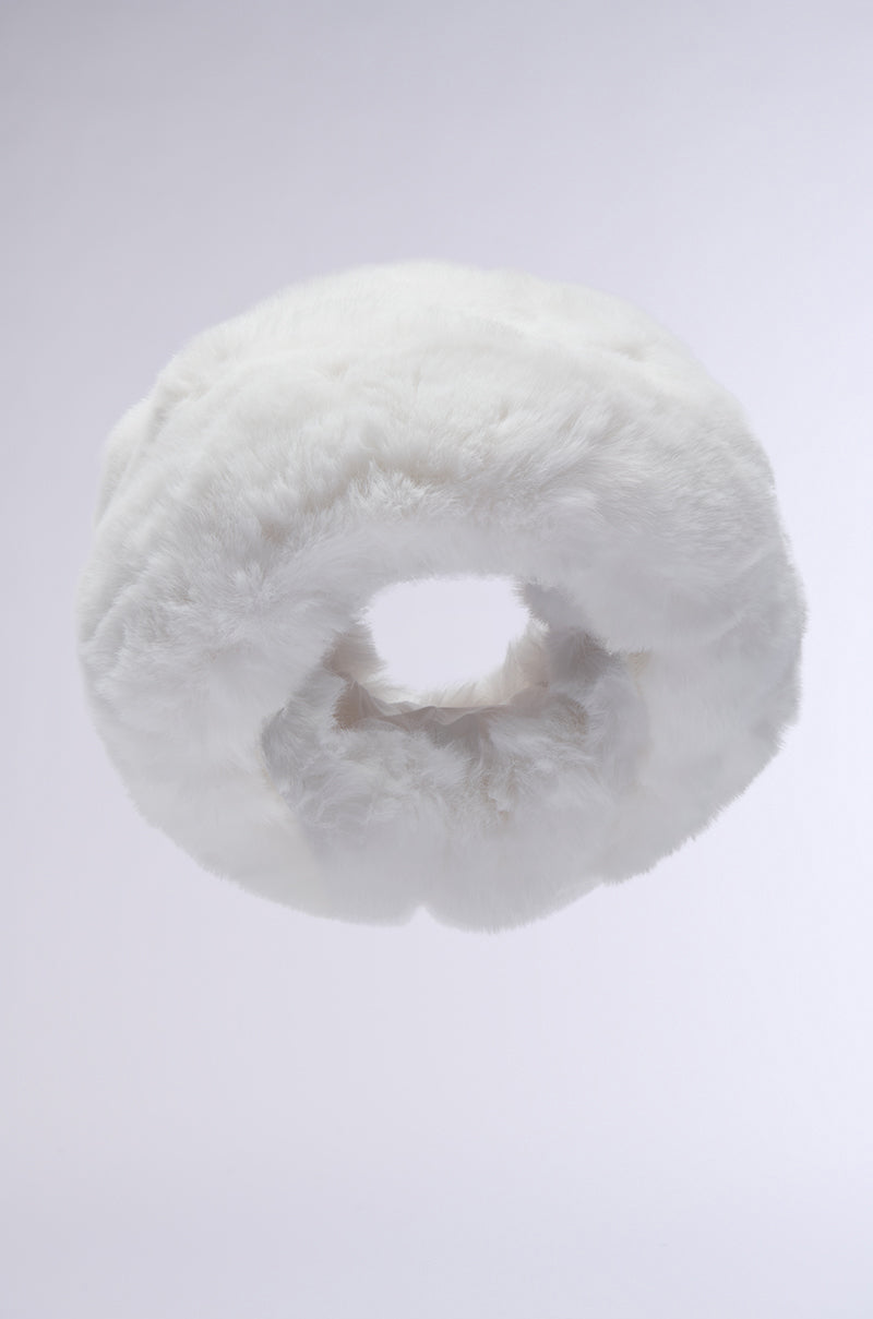 The LUXE JENNY FAUX FUR HEADBAND IN WHITE, a fluffy circular accessory, floats against a light gray background, resembling a soft winter headband.