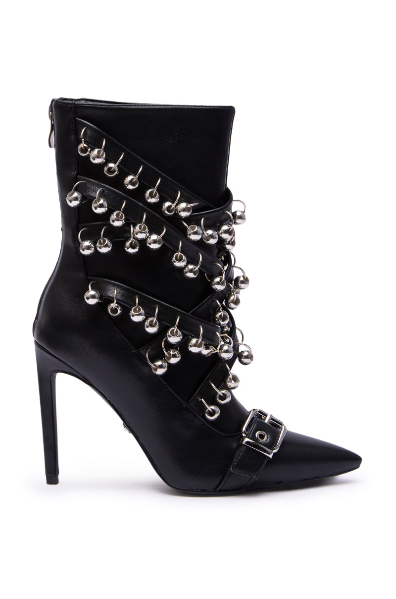 The AZALEA WANG HECATE BLACK METAL is a black faux leather stiletto boot with a pointed toe, crisscrossing straps adorned with silver bells, a stylish buckle near the toe, and an easy-access back zipper.