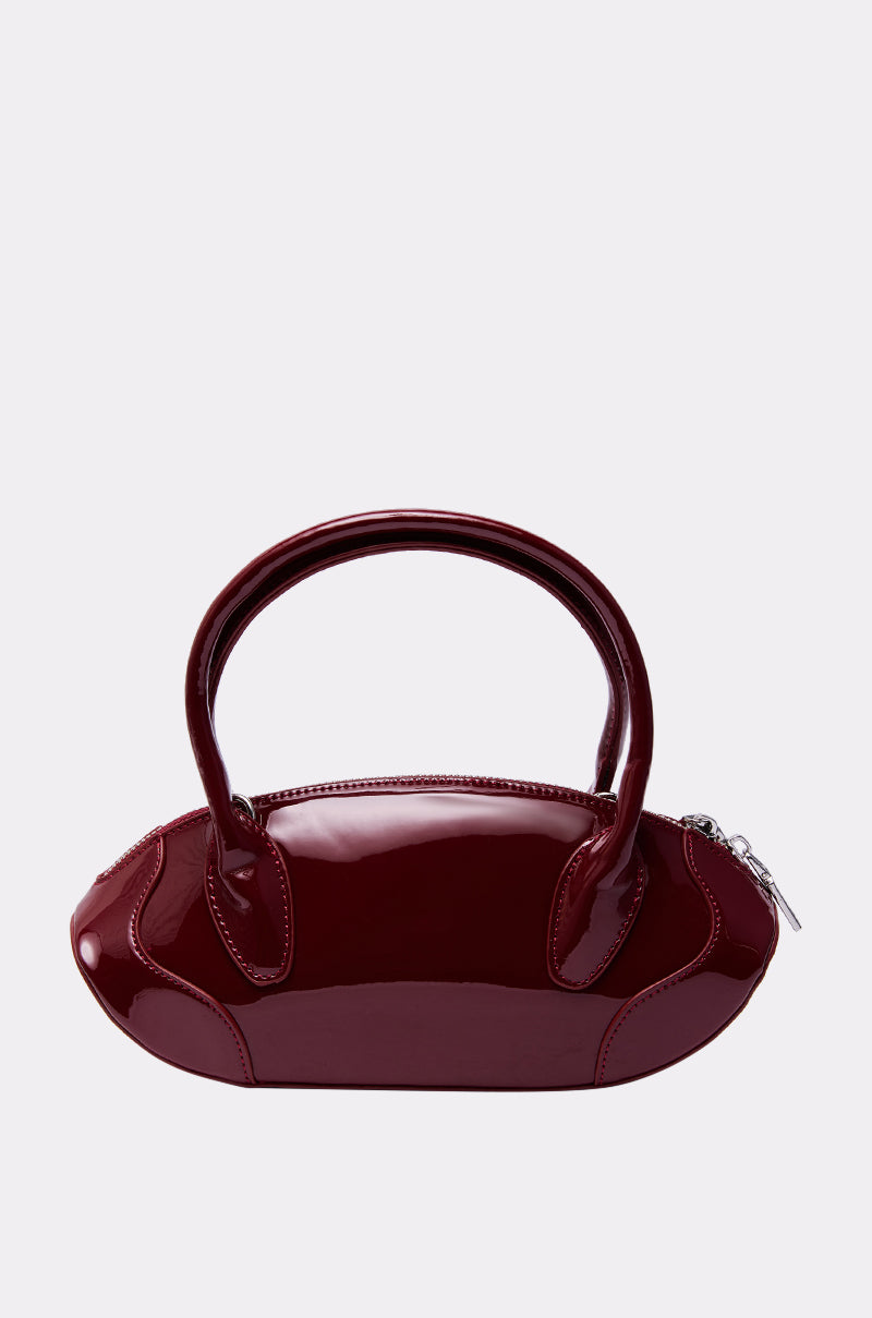 The BELLA PATENT PURSE is a glossy, dark red oval handbag with two rounded handles and a silver side zipper, shown on a plain light gray background.