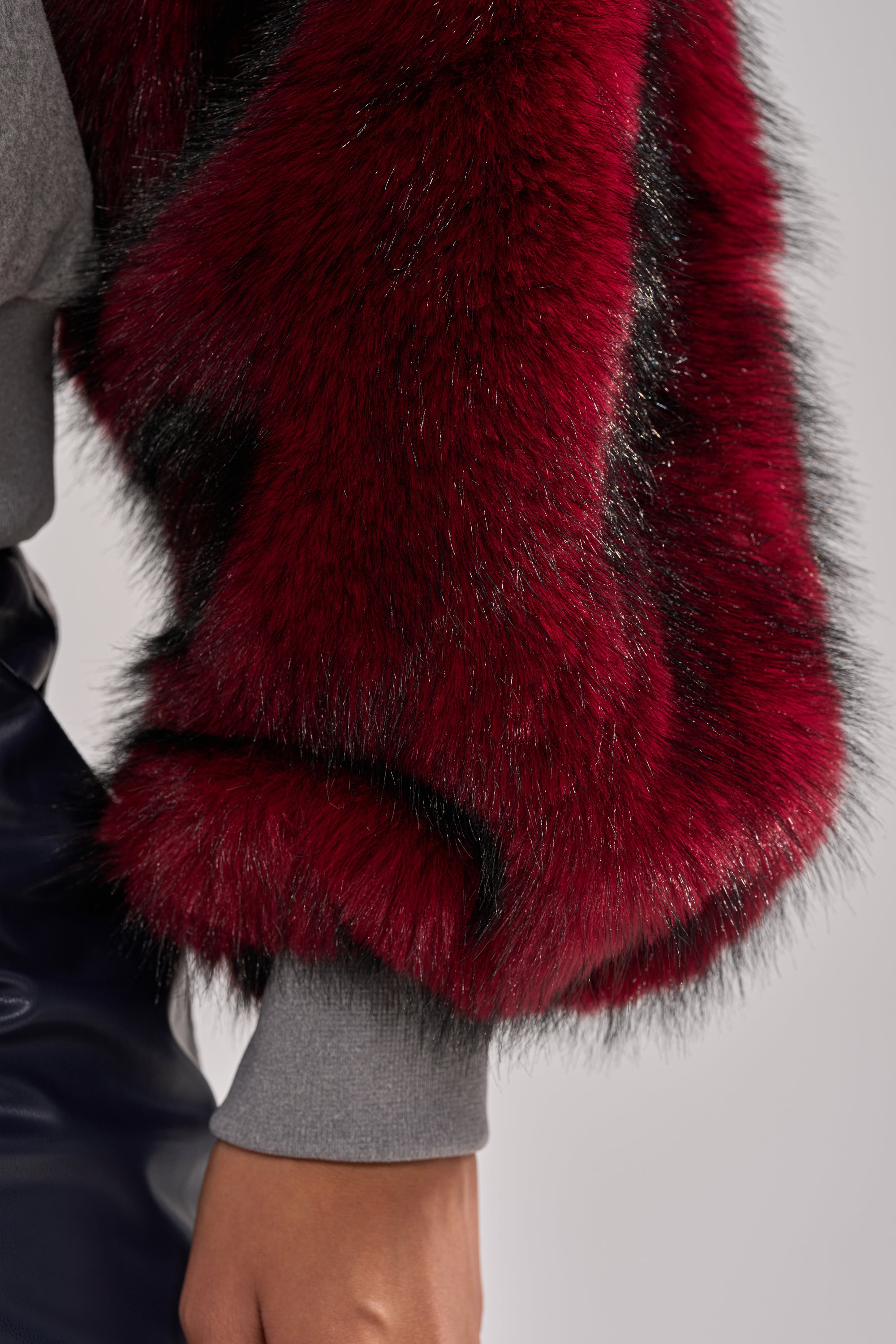 A close-up of a person in streetwear, wearing the NEW EAST SIDE FAUX FUR SLEEVE SWEATSHIRT over dark pants with their arm hanging by their side.