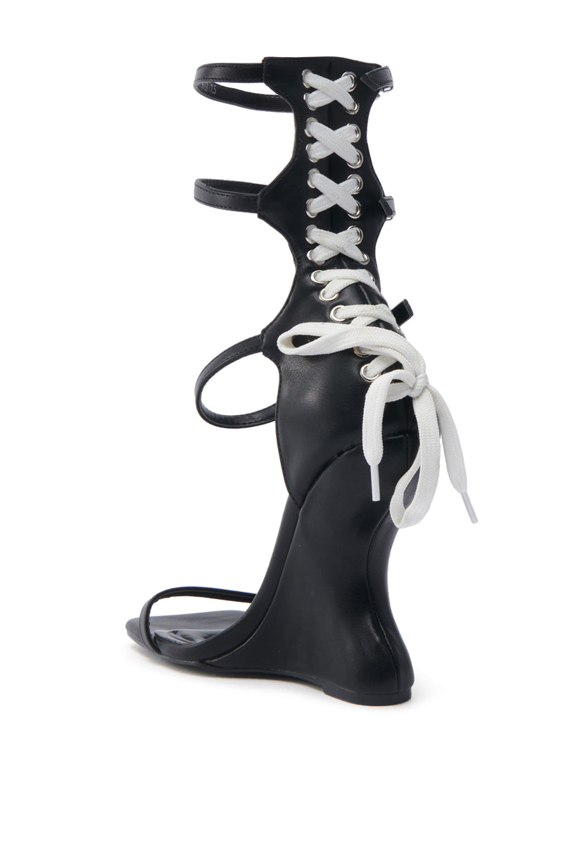 The AZALEA WANG ISAAK BLACK WITH WHITE LACES WEDGE SANDAL features a chic faux leather design, unique back lacing with white bow-tied laces, an open square toe, and a high sculpted heel. This stylish sandal is completed with ankle and toe straps.