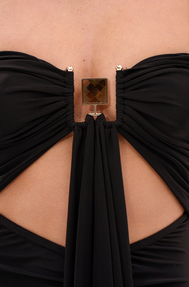 Close-up of the ONE OF A KIND CUTOUT JUMPSUIT in black, featuring luxe stretch fabric, ruched details, and a gold square gemstone clasp at the center that creates a daring cutout beneath the chest.