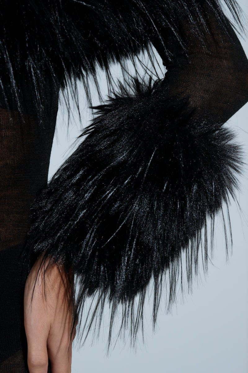 Close-up of an individual wearing the STAR OF THE SHOW FUR MINI DRESS, featuring fluffy faux fur cuffs that contrast with the black sheer knit fabric. This elegant design showcases a strapless neckline against a light background.