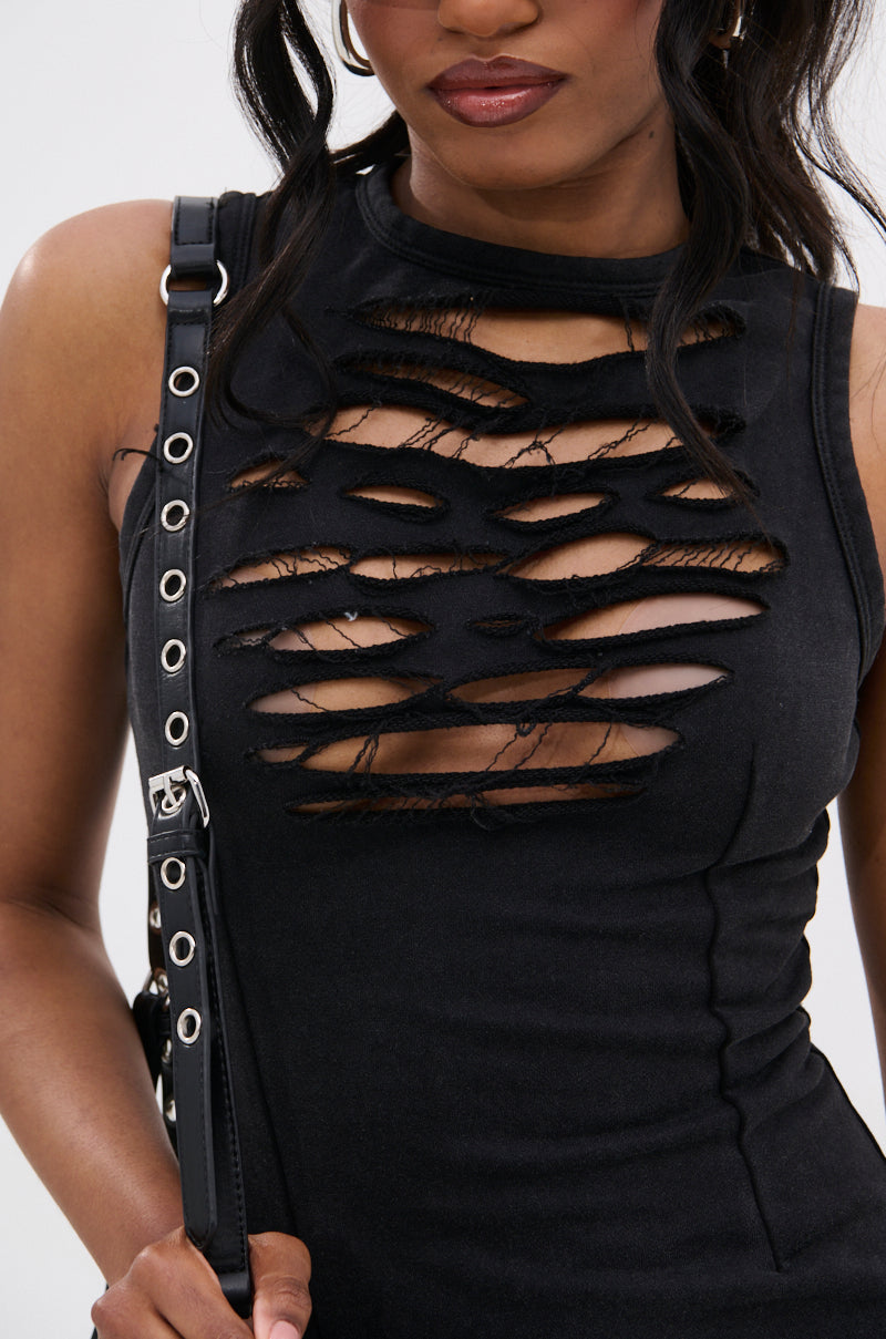 A woman wears the DIXIE SHREDDED MINI DRESS, a sleeveless black dress with curve-hugging fit and chest cutouts, paired with a black shoulder bag featuring silver grommets. Only her upper body is visible.