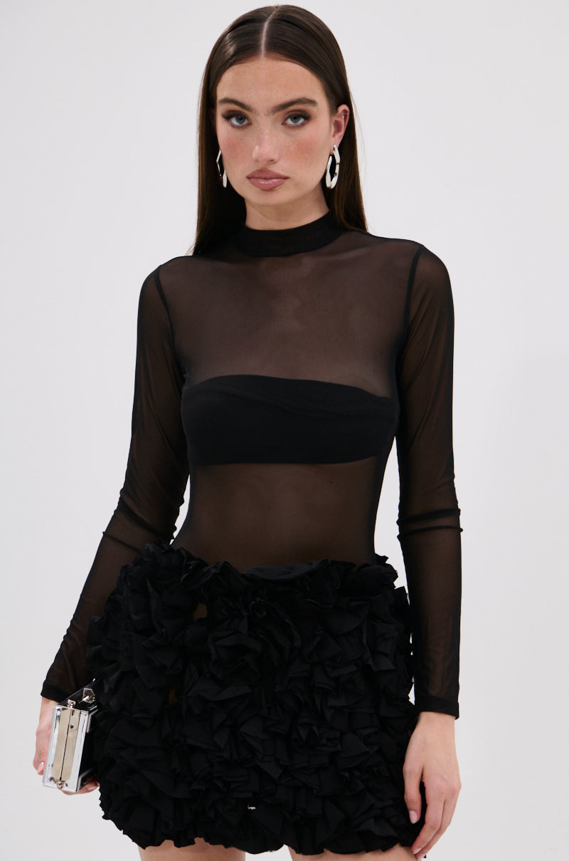 She radiates sophistication in the KELYN Mesh Mini Dress in Black, styled with straight hair, hoop earrings, and a small metallic handbag.