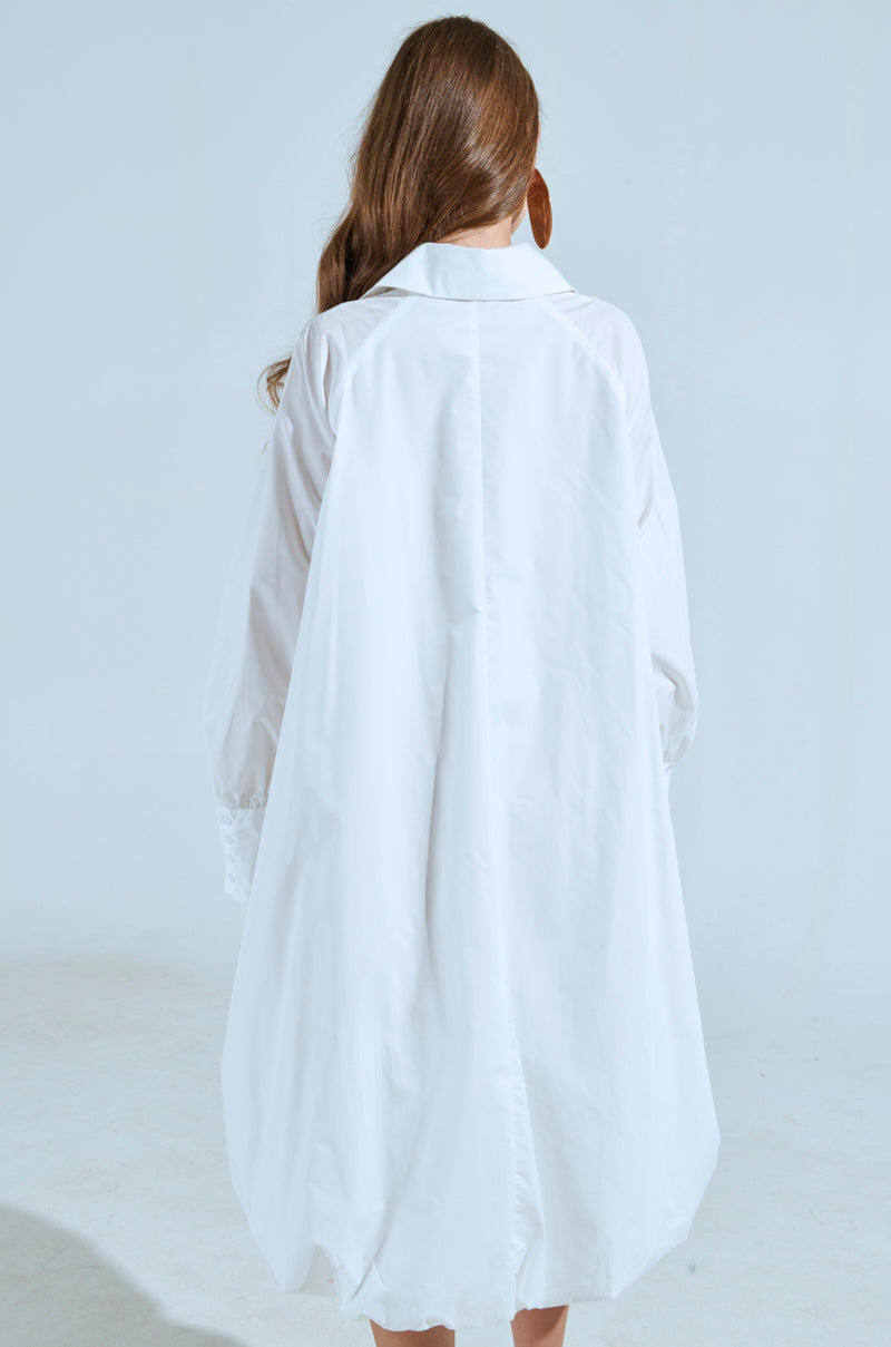 A woman with long hair stands with her back to the camera, wearing the oversized SHE MEANS BUSINESS MINI DRESS. The background is plain and light-colored, highlighting the simplicity and elegance of her outfit.