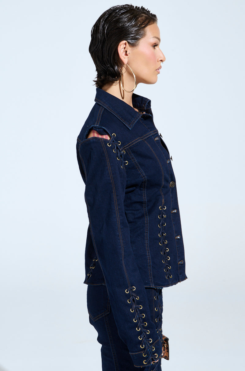 A model with short dark hair and large hoop earrings showcases the chic "THATS ON ME BUTTON DOWN TOP," a denim shirt featuring lace-up detailing on the sides and sleeves, set against a light gray background.