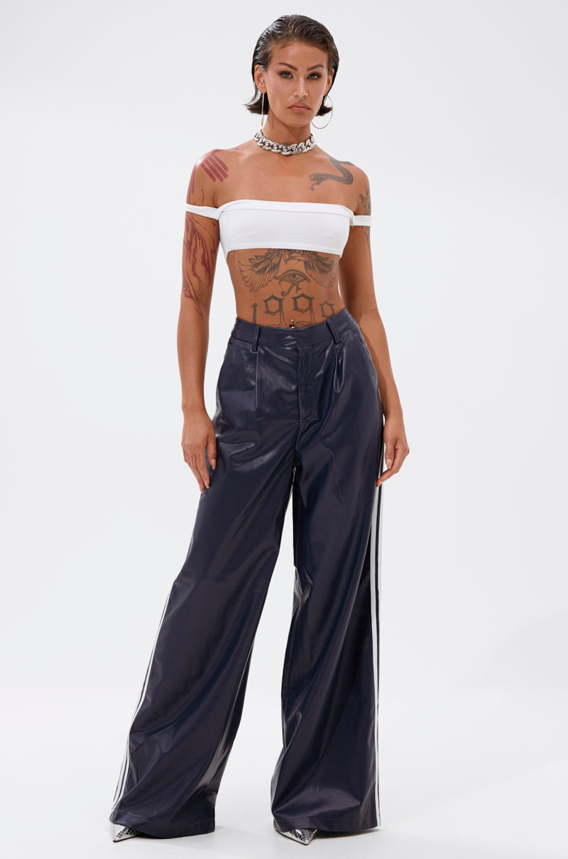 A person with wet-look hair wears a white off-the-shoulder bandeau top and the DAYTIME LOVIN TROUSER IN NAVY. They show off visible arm and torso tattoos and accessorize with a chunky silver chain necklace.