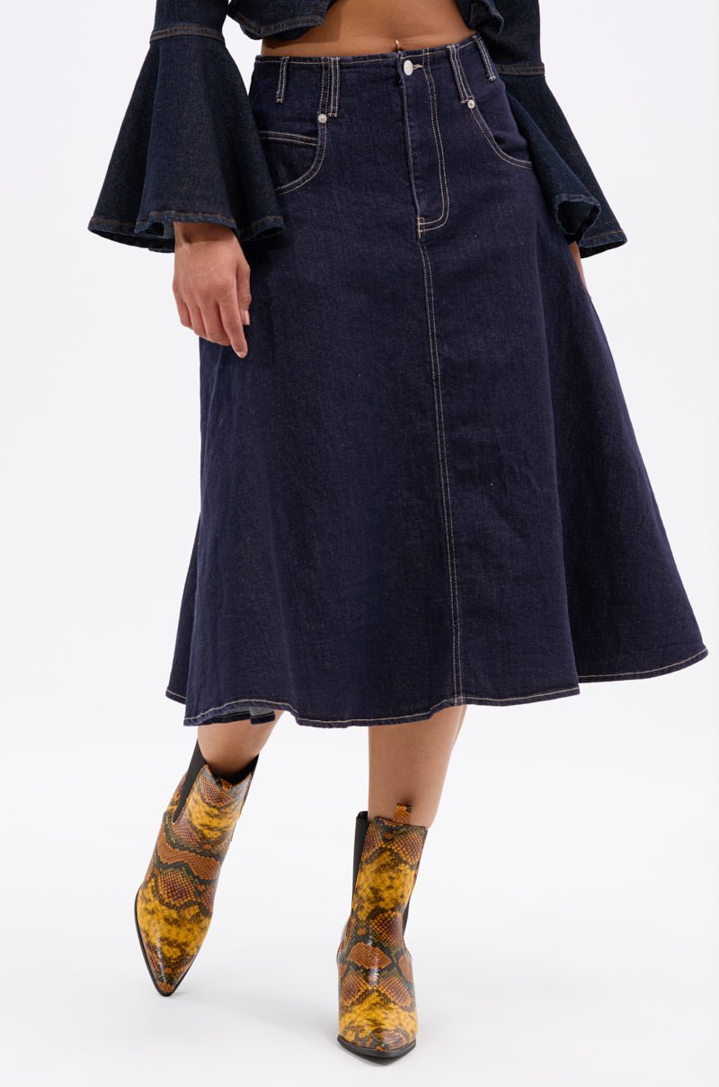 Person wearing the COME WITH ME DENIM MIDI SKIRT—dark denim, A-line silhouette, contrast stitching—paired with a matching flared-sleeve jacket and yellow-brown snakeskin ankle boots, standing against a plain white background.