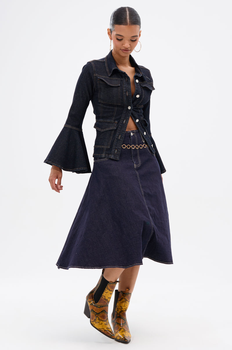 A woman stands against a plain white background wearing the COME WITH ME DENIM MIDI SKIRT, a dark-wash denim jacket with flared sleeves, and yellow snakeskin ankle boots.