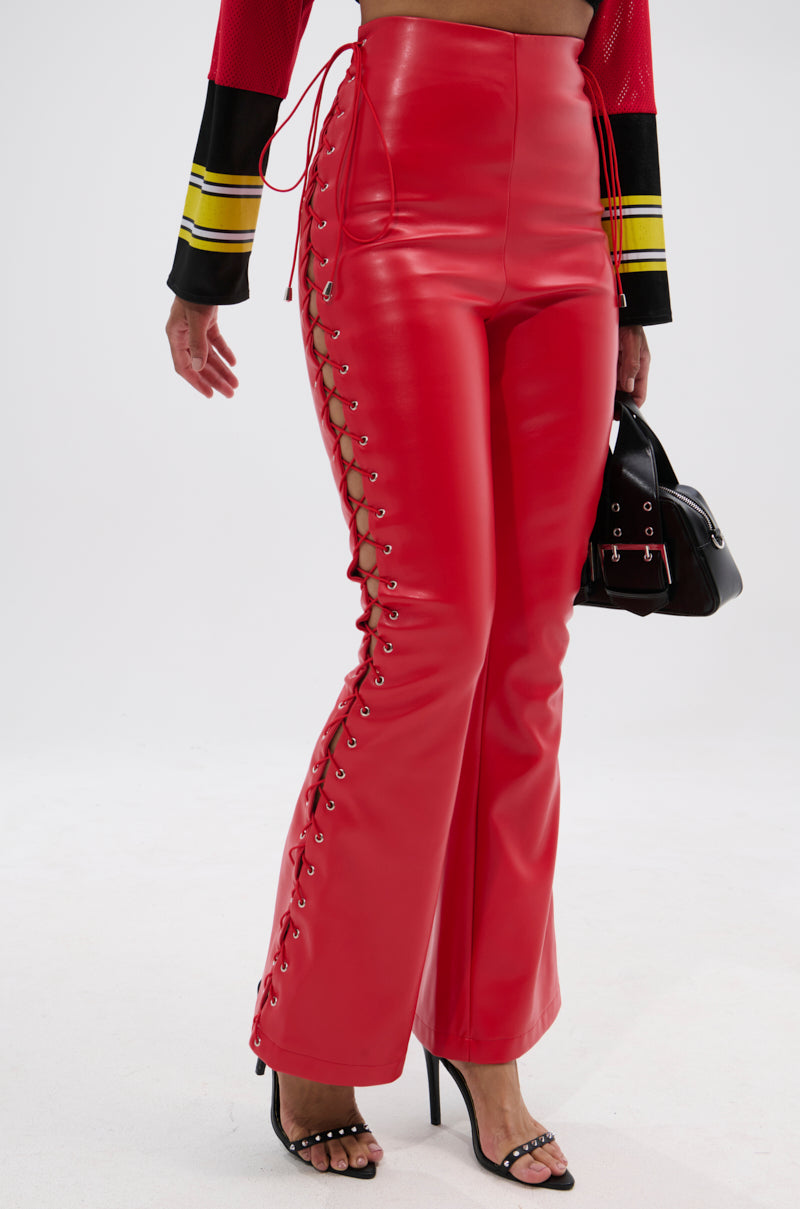 Model wears SEXY FAUX LEATHER RED LACE-UP PANTS with black heeled sandals, a cropped red and black top, and holds a small black handbag against a plain white background.
