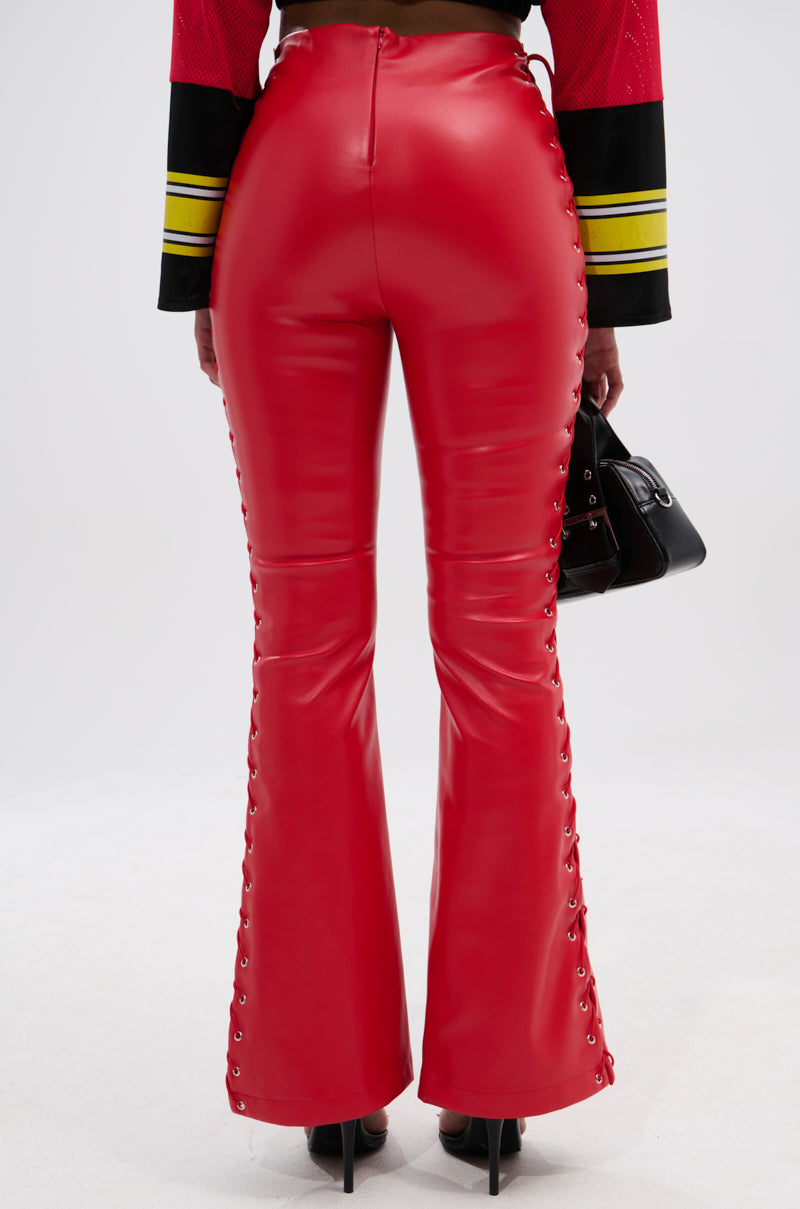 Wearing SEXY FAUX LEATHER RED LACE-UP PANTS and a sporty red and black long-sleeve top, a person stands in high heels with a small black handbag, photographed from the back.