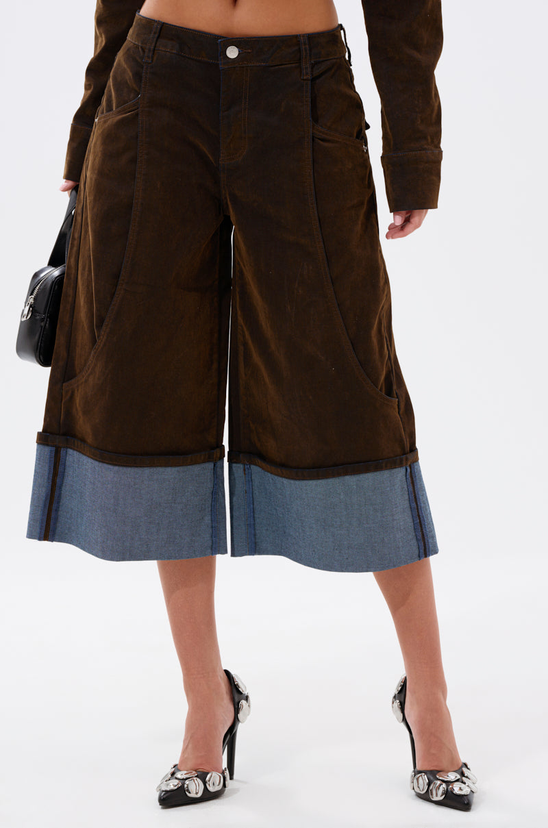 Someone models the FALL VIBES VELVET BERMUDA SHORT, paired with a black handbag and black high heels featuring round silver embellishments, against a plain white background.