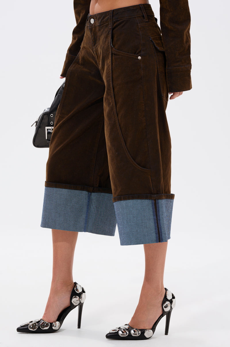 A person wears the FALL VIBES VELVET BERMUDA SHORT with a matching brown jacket, black high heels featuring silver buckles, and carries a small black handbag—ideal for chic fall style.