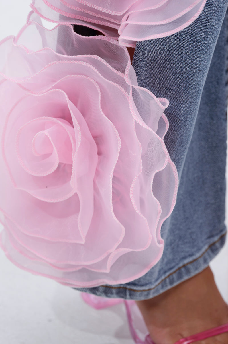Close-up of the FLOWER GIRLIE APPLIQUE DENIM JEANS featuring sheer pink organza flower-shaped ruffles at the high-rise, wide-leg hem, with a pink sandal visible below.