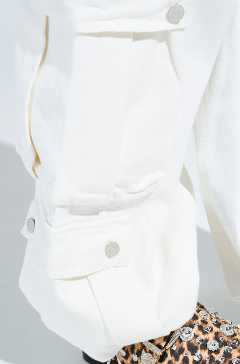 Close-up of a GET RIGHT TO IT CARGO DENIM PANT pocket with silver buttons, paired with a peek of a studded leopard print shoe.