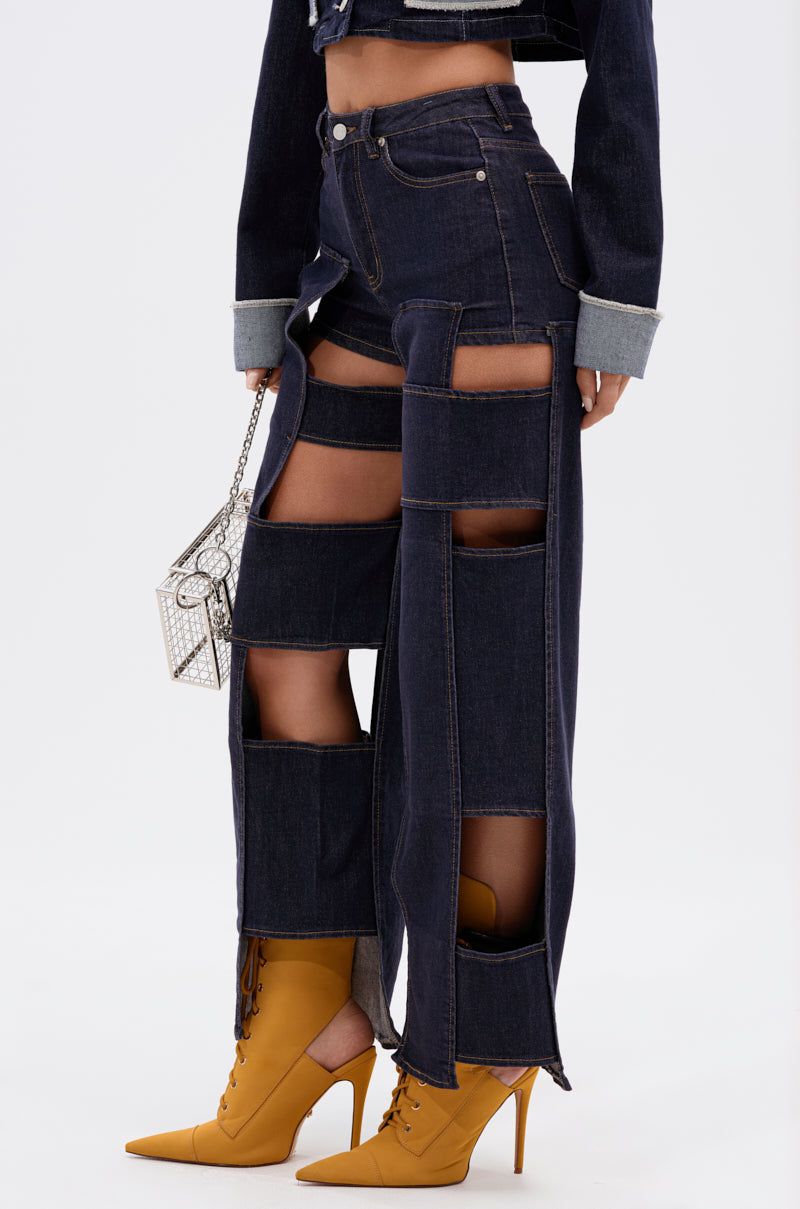 Wearing the LOCKED UP FOR GOOD DENIM PANT featuring high-rise cut-outs with denim shorts underneath, paired with a small silver purse and mustard yellow lace-up heeled boots.