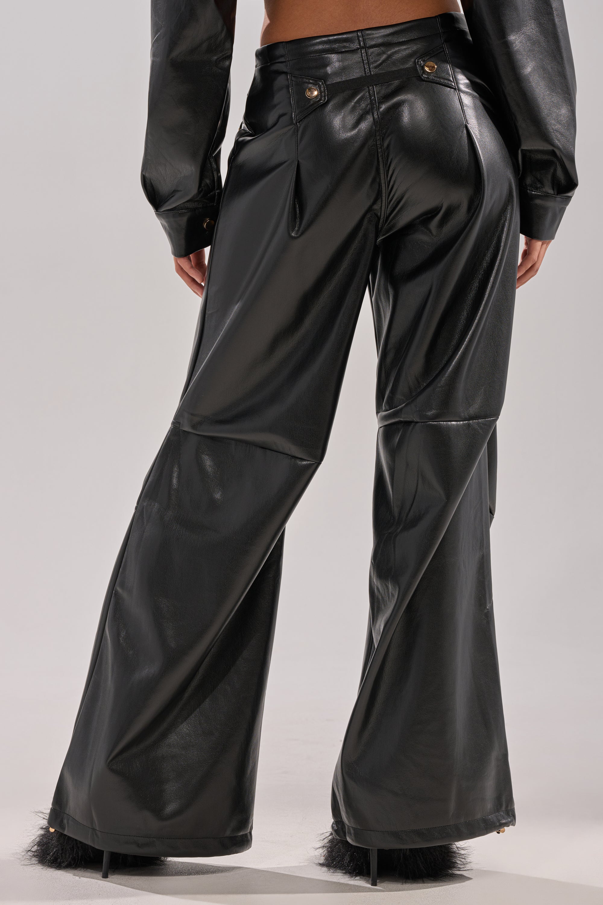 A person wearing the GET WITH IT FAUX LEATHER TROUSER in black, high-rise fit with a wide-leg design and a matching long-sleeve top, seen from the back against a plain gray background.