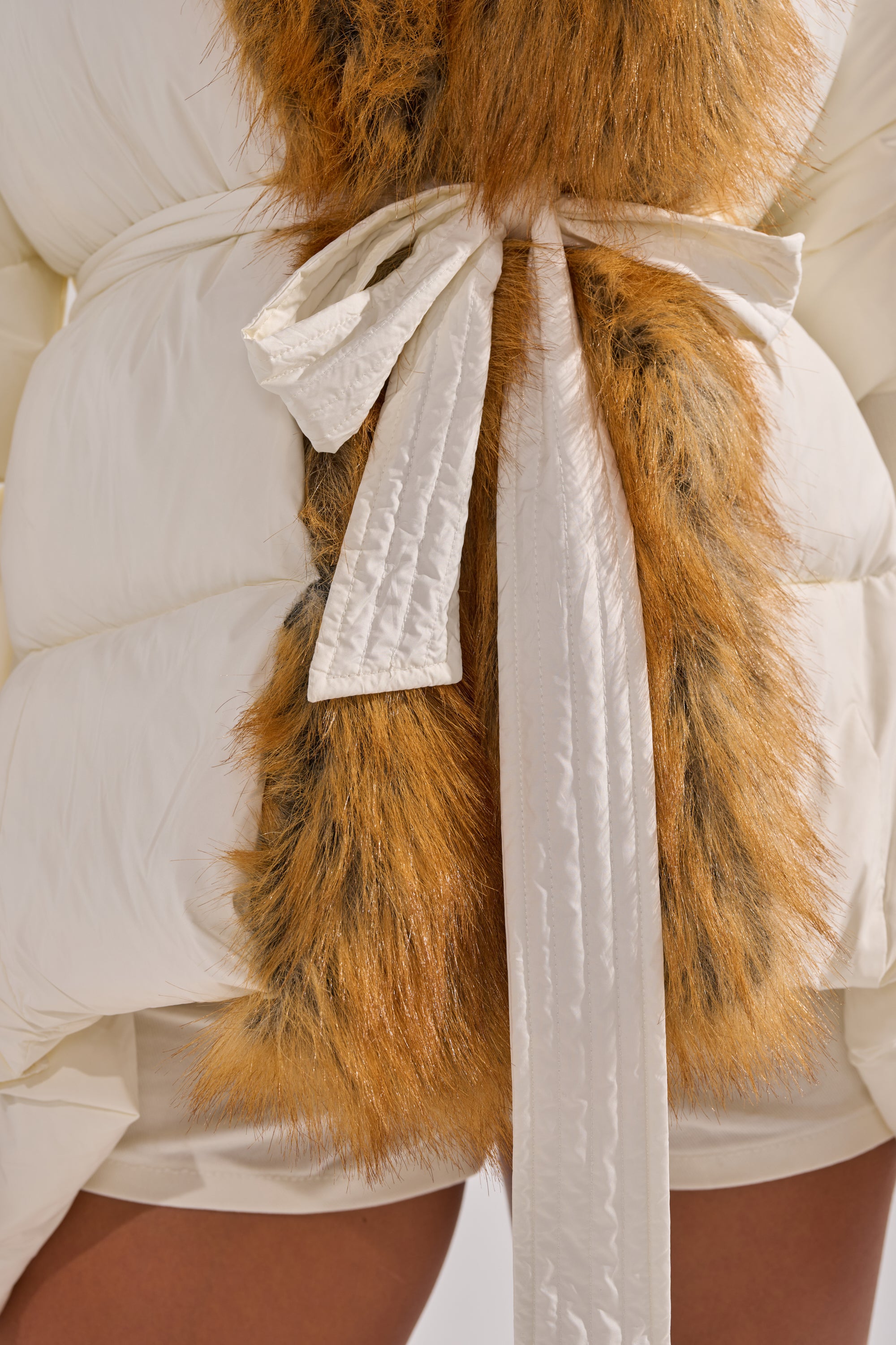 Close-up of a person wearing the TALK TO ME NICE FUR TRIM PUFFER, a white quilted coat with a fabric belt and a luxurious brown and black faux fur collar that adds drama to its peplum silhouette.