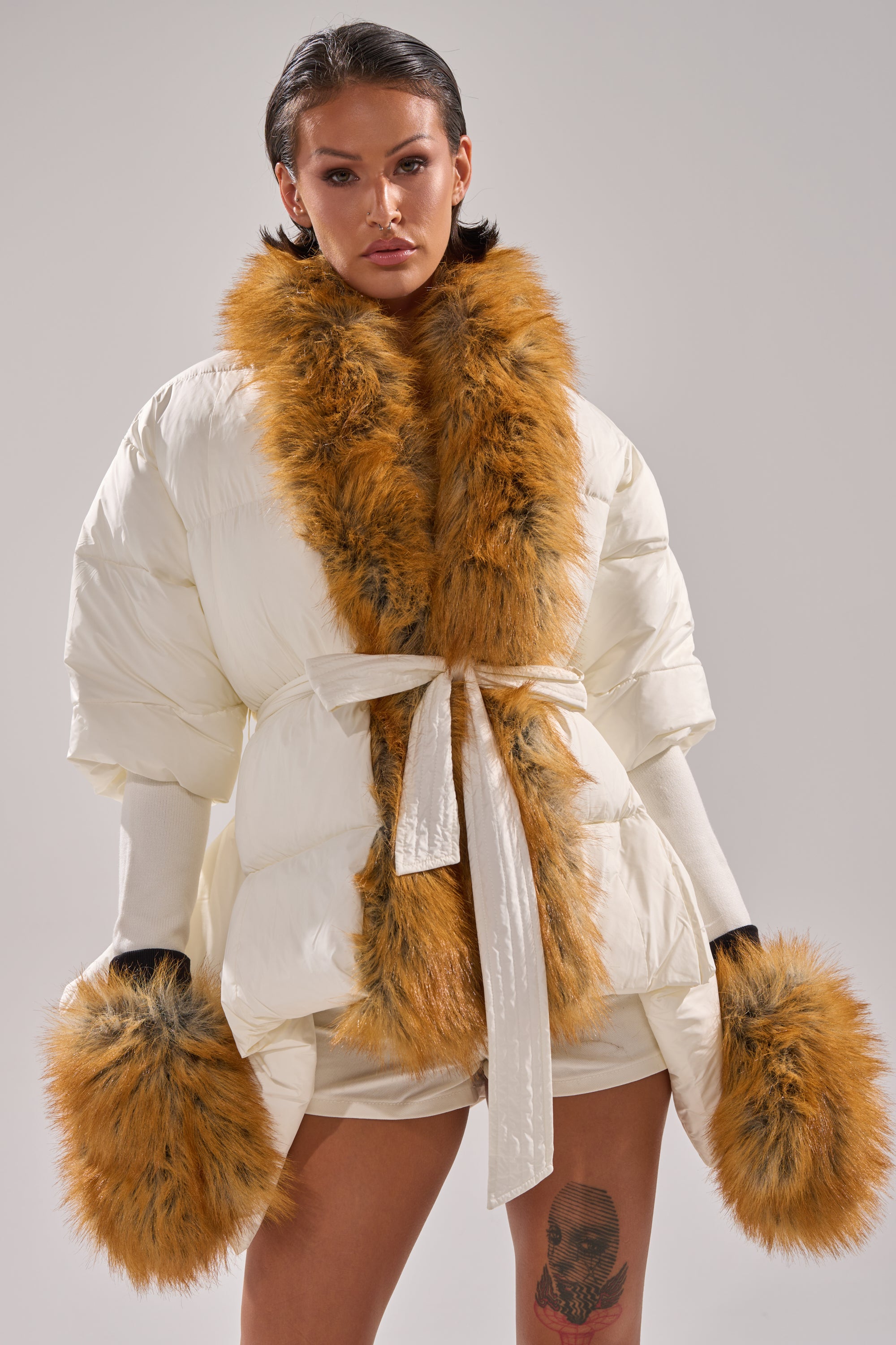 A person models the TALK TO ME NICE FUR TRIM PUFFER, featuring a white body with bold orange faux fur collar and matching cuffs, posing confidently against a plain light gray background.