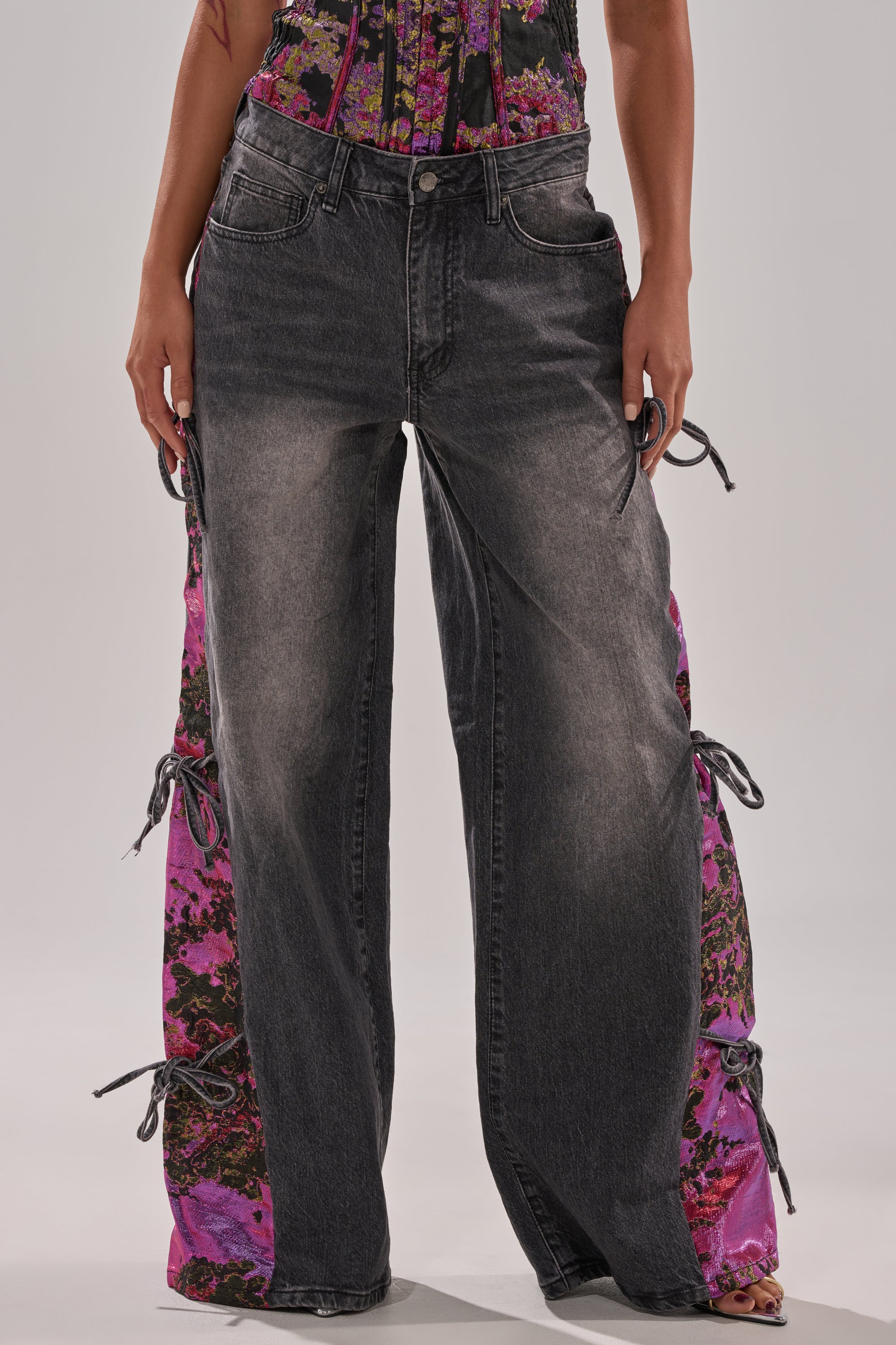 Someone wearing the LETS PARTY BROCADE RELAXED DENIM—wide-leg, faded black jeans with vibrant pink floral brocade panels and side ties—paired with a matching floral top.
