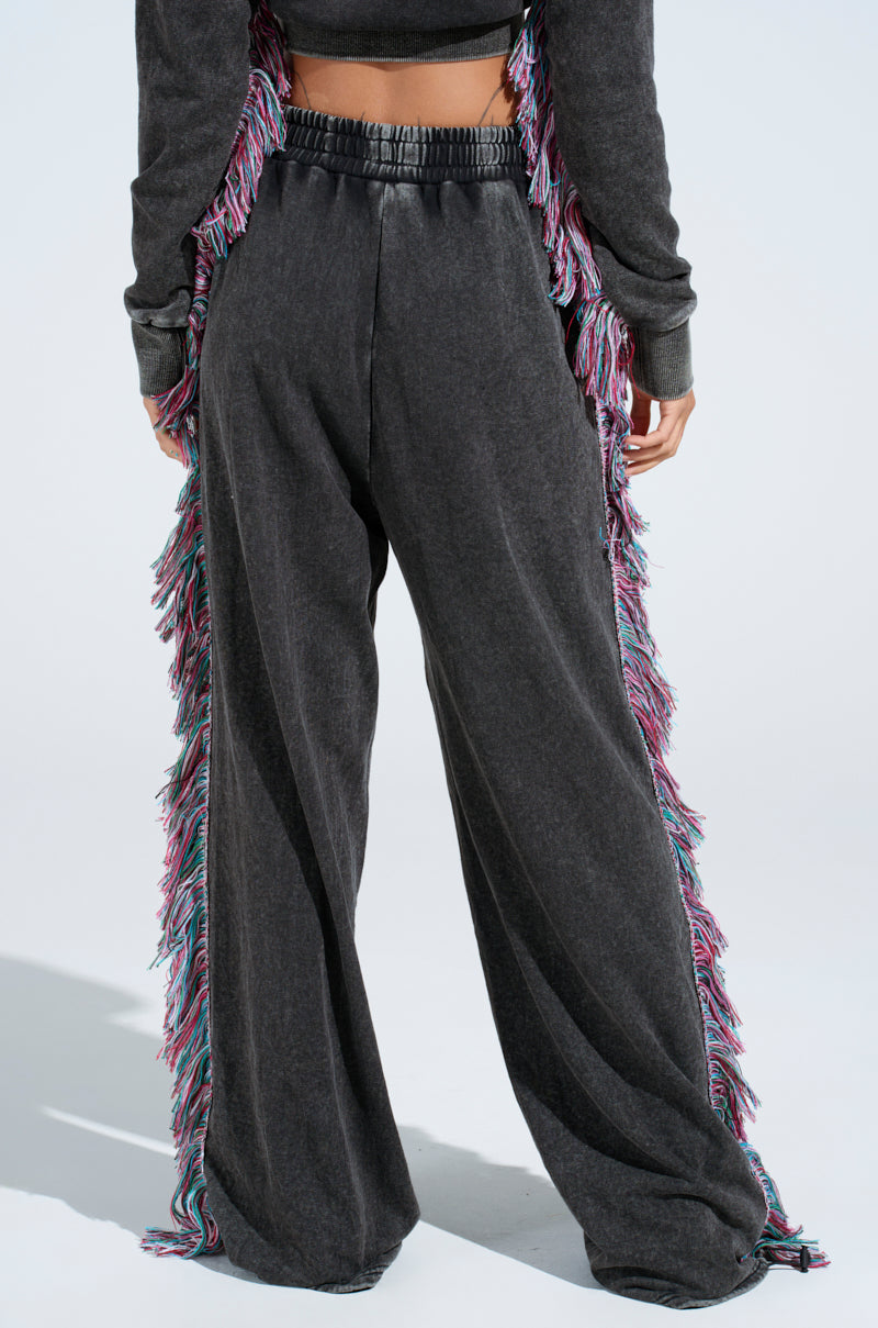 Someone is wearing THE ONE AND ONLY JOGGER in dark gray with colorful fringe on the sides. These cotton-blend joggers feature a high elastic waistband, paired with a matching top against a plain light background that highlights the vibrant design.