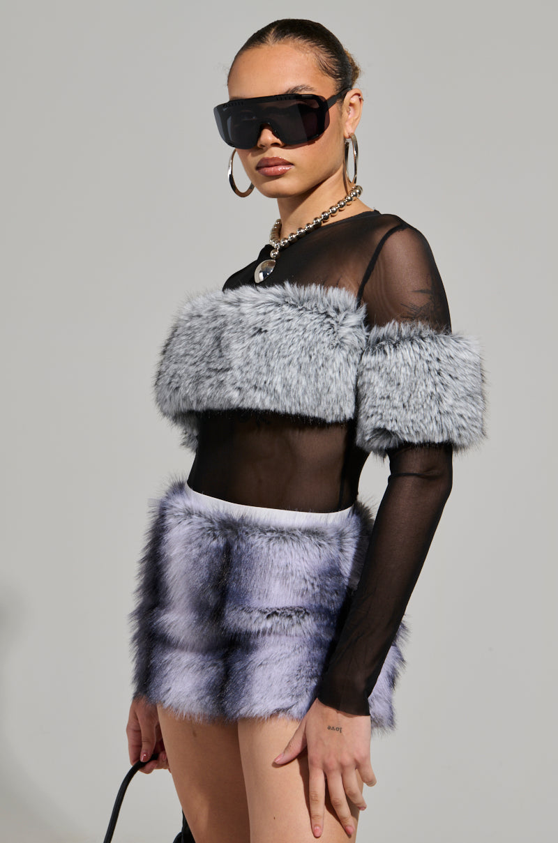 A person is wearing the JENNY LONG SLEEVE TOP WITH FUR, featuring black sheer fabric and gray faux fur accents, teamed with a short gray fur skirt. They accessorize with oversized black sunglasses, hoop earrings, and a chunky necklace, set against a plain, neutral background.