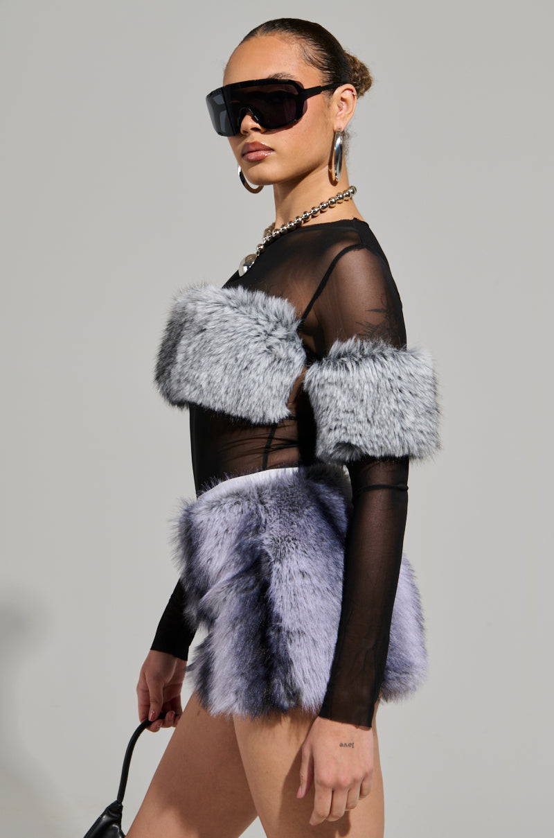 A person dressed in a fashionable outfit showcases the JENNY LONG SLEEVE TOP WITH FUR, a sheer, stretchy mesh black top paired with a fluffy faux fur-like gray skirt featuring shoulder accents. They wear large black sunglasses and hoop earrings, posing confidently against a plain backdrop and embodying chic style.