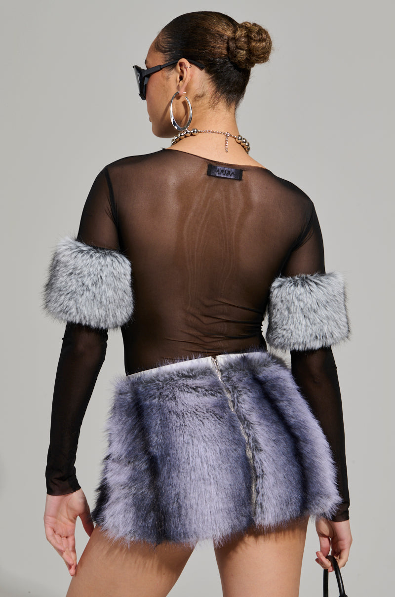 A person with their back to the camera models a Jenny Long Sleeve Top with Fur, styled in stretchy mesh, and paired with a short purple faux fur mini skirt. They complete the chic look with sunglasses, hoop earrings, a necklace, and their hair elegantly styled in a bun.