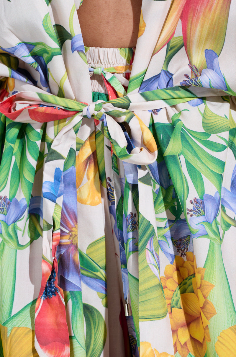 Close-up of the INTO THE GARDEN CARDIGAN, featuring a tropical floral print with green leaves and colorful flowers. The lightweight fabric is tied in a bow and appears to be part of a garment worn by a person.