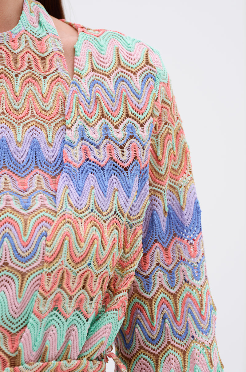 Close-up of the TAKE ME TO MIAMI DUSTER, featuring a colorful wavy crochet pattern in pastel green, blue, pink, and beige shades. The detailed texture and vibrant design offer a chic, resort-ready style.