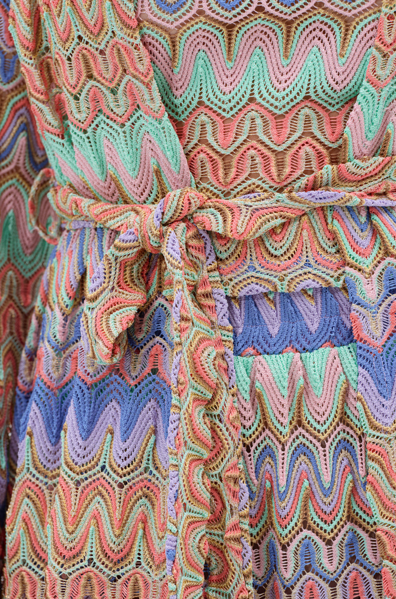 Close-up of the TAKE ME TO MIAMI DUSTER, showcasing its wavy pastel patterns in pink, green, blue, purple, and yellow. This textured fabric duster features a matching belt at the waist—ideal for your next resort escape.