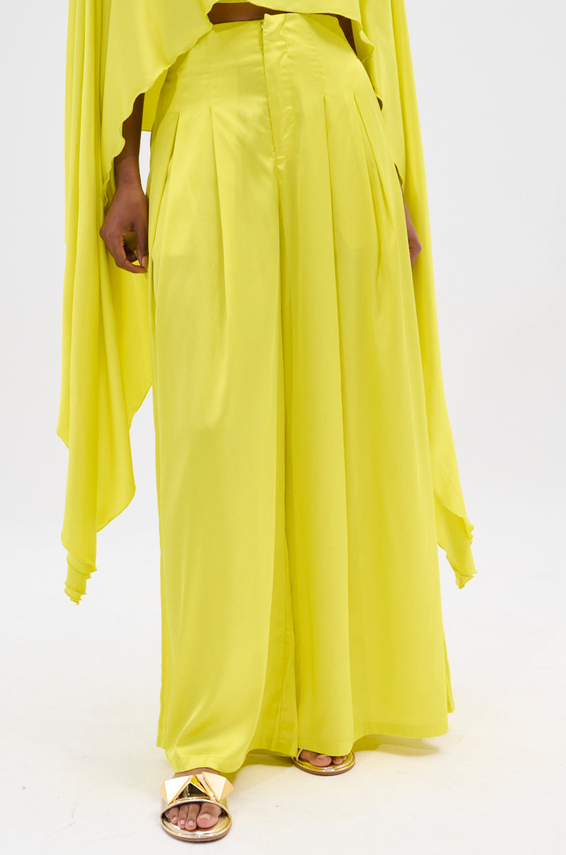 A person stands against a plain white background wearing bright yellow COCKTAIL HOUR WIDE LEG PANT and a matching flowing top, paired with gold sandals.