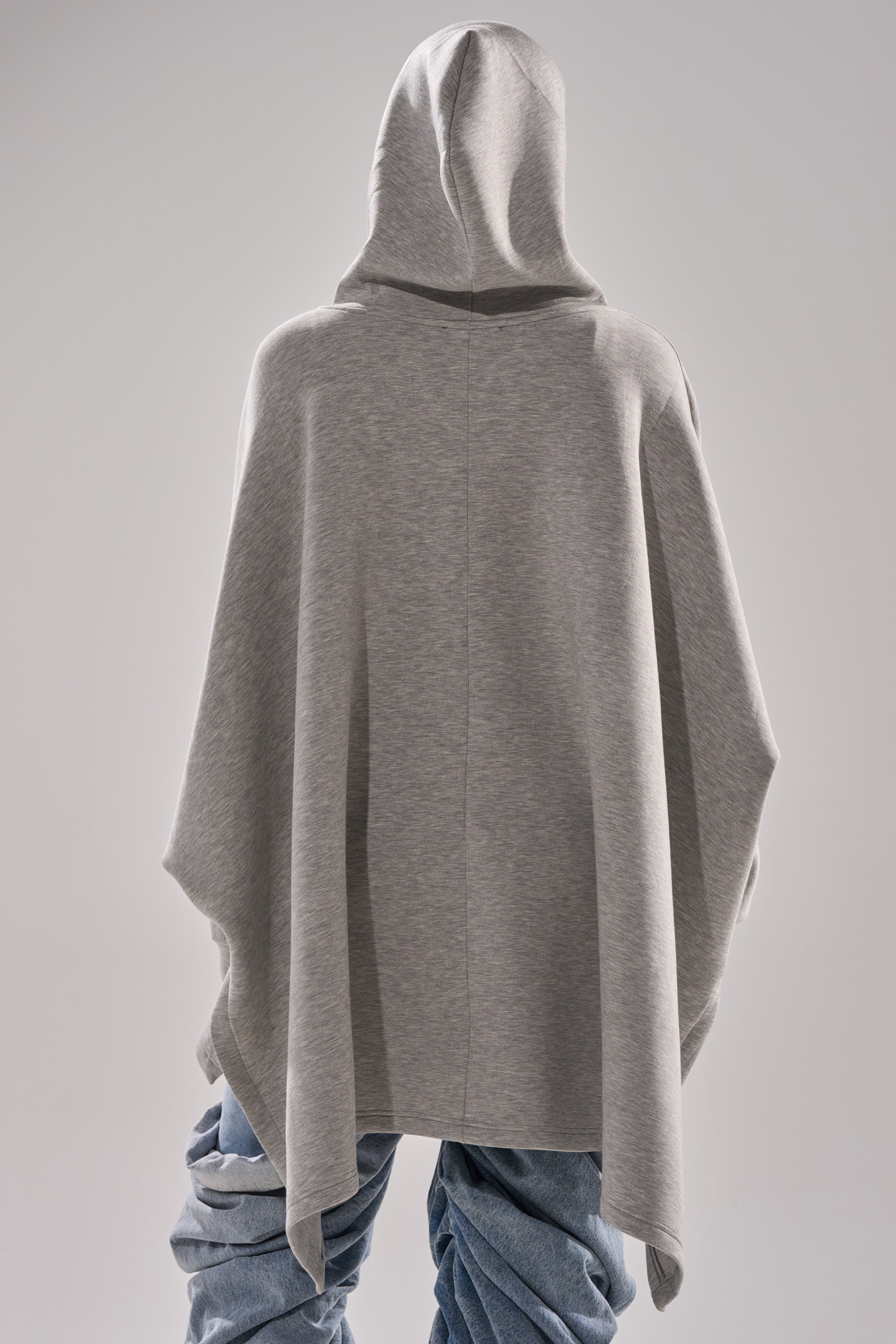 A person faces away, wearing the CREW LOVER OVERSIZED ZIP UP SWEATSHIRT in heather grey styled as a loose hoodie with baggy, twisted blue jeans against a plain light gray background.