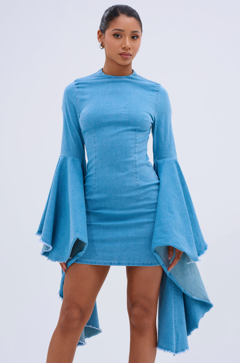 A woman models the SHE'S ROYAL DENIM LONG SLEEVE MINI DRESS, a bodycon mini in light blue denim with dramatic bell sleeves and an asymmetric hem, against a plain light background.